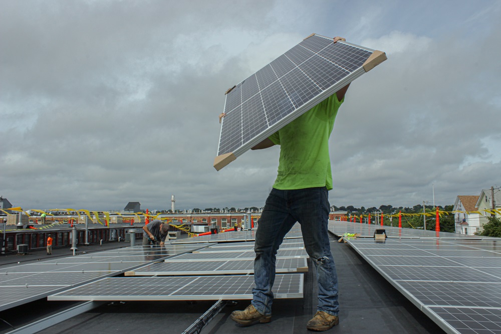 Construction worker carries solar panel across commercial flat roof