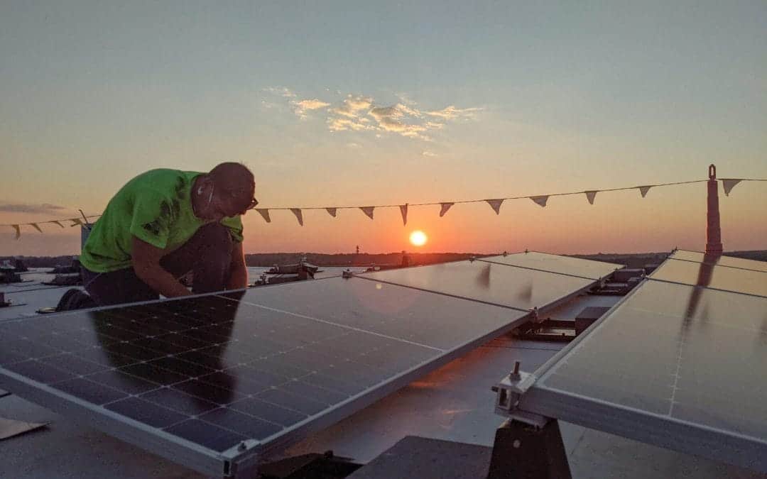 Man installs commercial solar panels on a roof with sun setting in background
