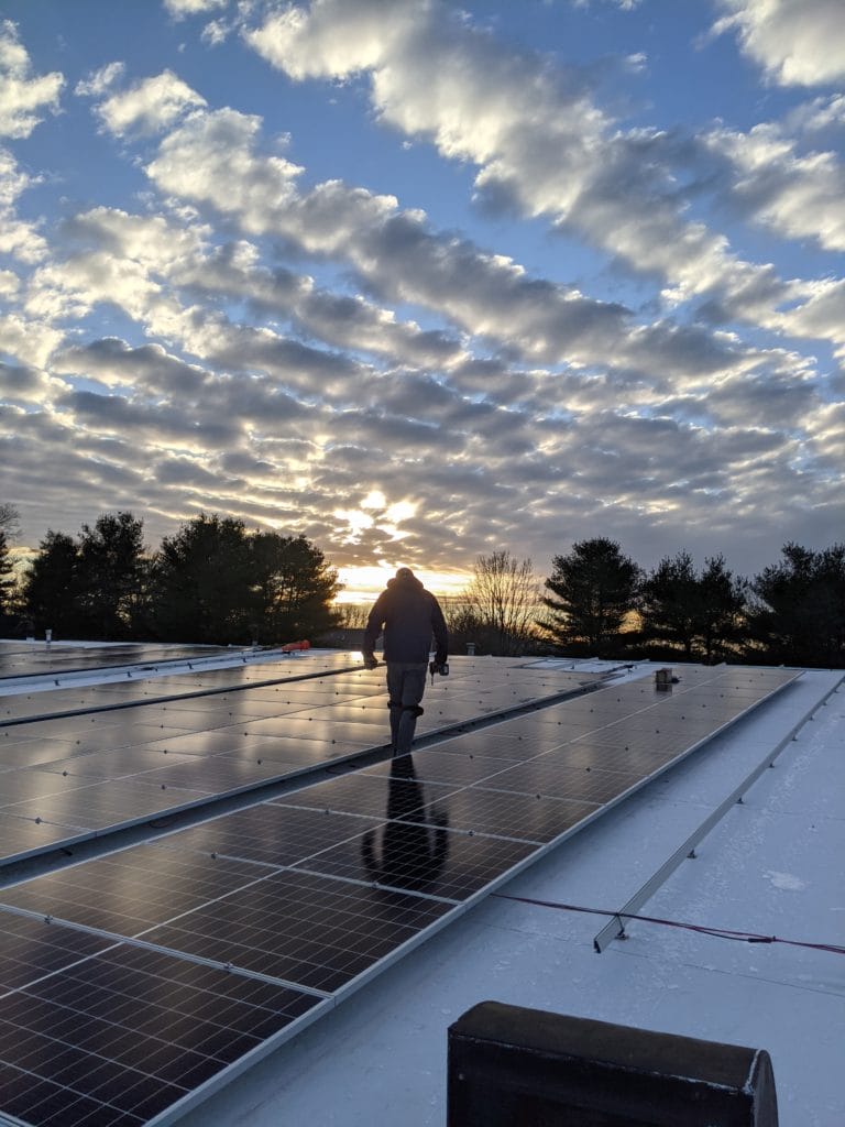 Solar installer walks among rows of solar panels at sunrise