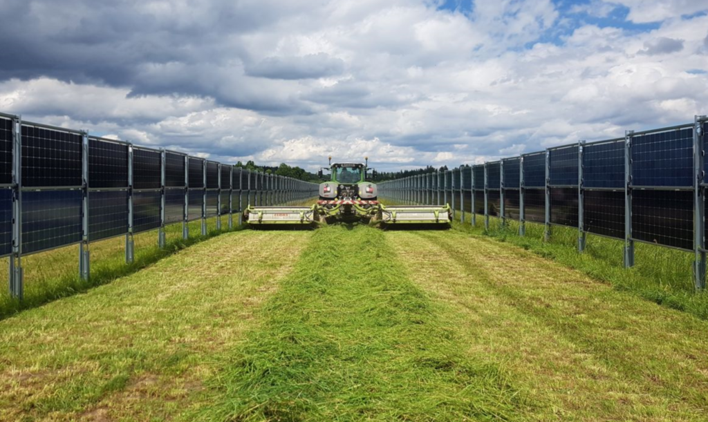 Picture of farmer mowing grass between vertical bifacial solar panels. Solar farm land lease rates Pennsylvania