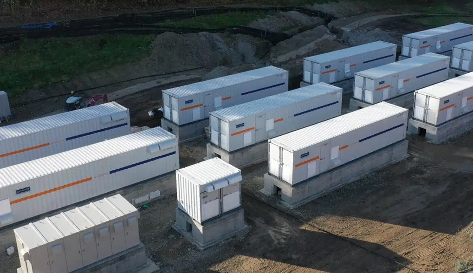 This image shows the 24 hour solar power plant's battery storage containers. They are placed on concrete foundations and the dirt has been excavated around the foundations to facilitate electrical connections. When the connections are complete they will backfill the area.