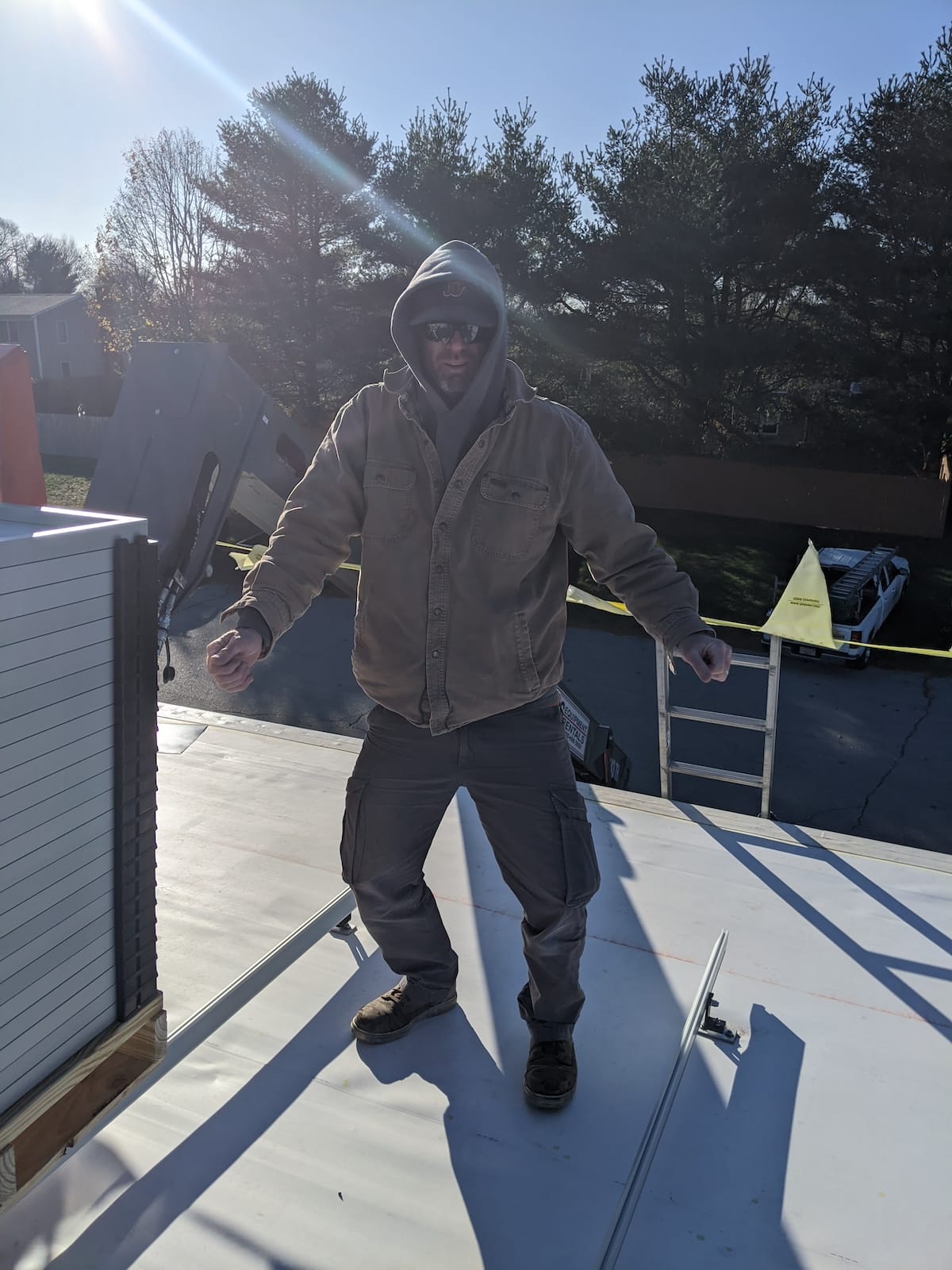 Solar installer on white TPO roof with ladder and pallet of solar panels