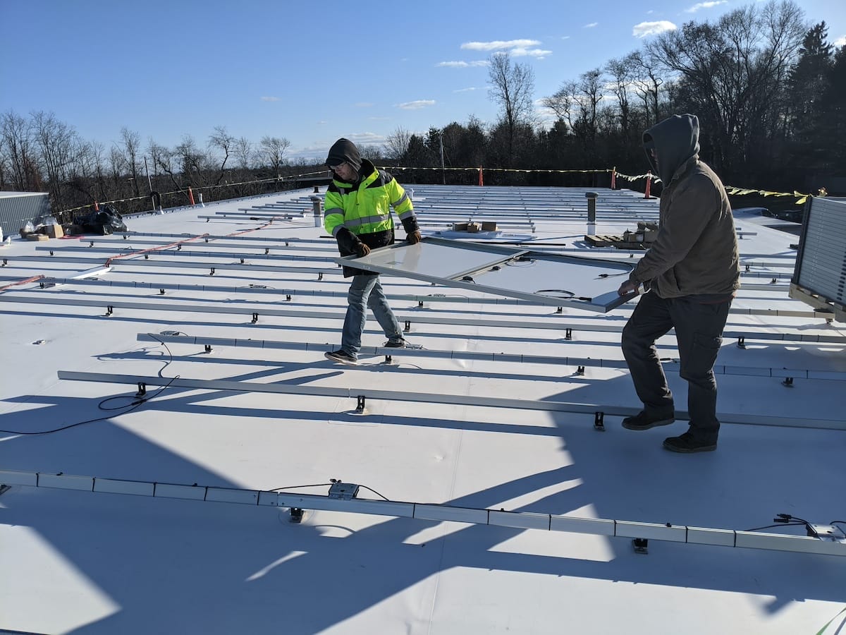 Solar installers carrying panel across white TPO rooftop