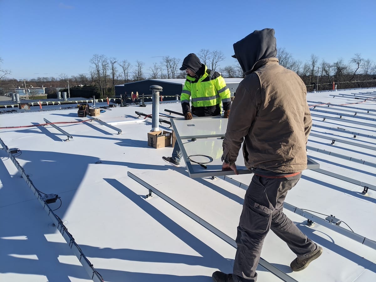 Solar installers carry panel across white TPO rooftop 