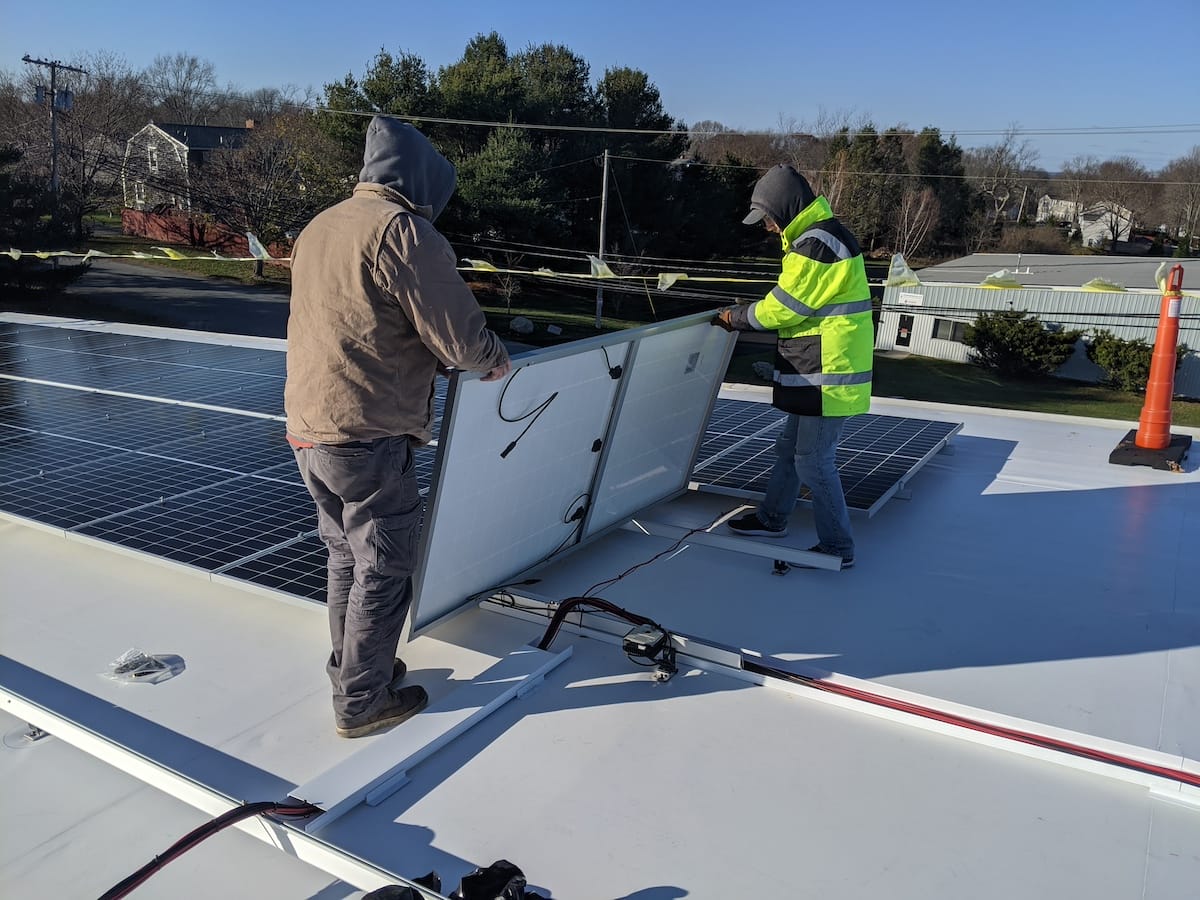 Workers place panel on Ironridge extrusions for commercial solar install