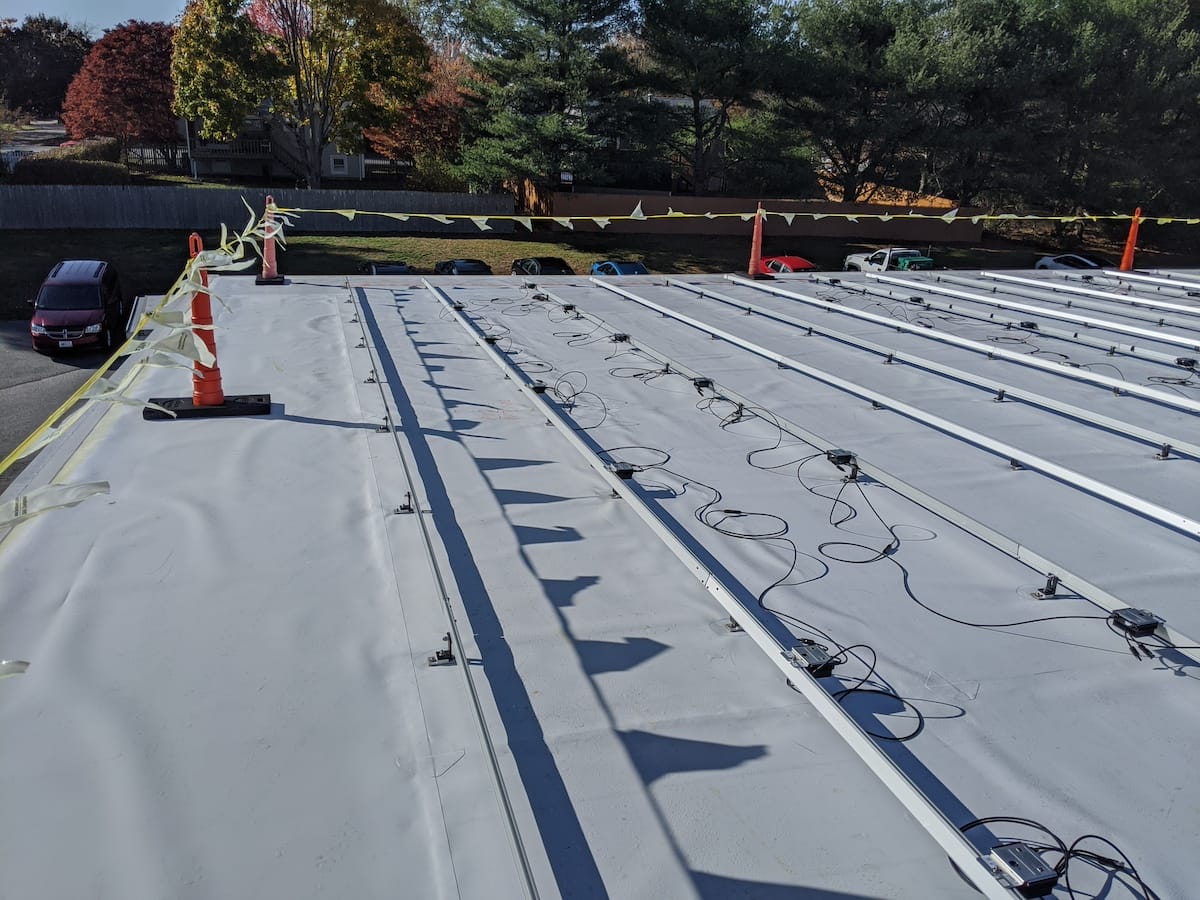 Optimizer installation on extruded rails above white TPO roofing