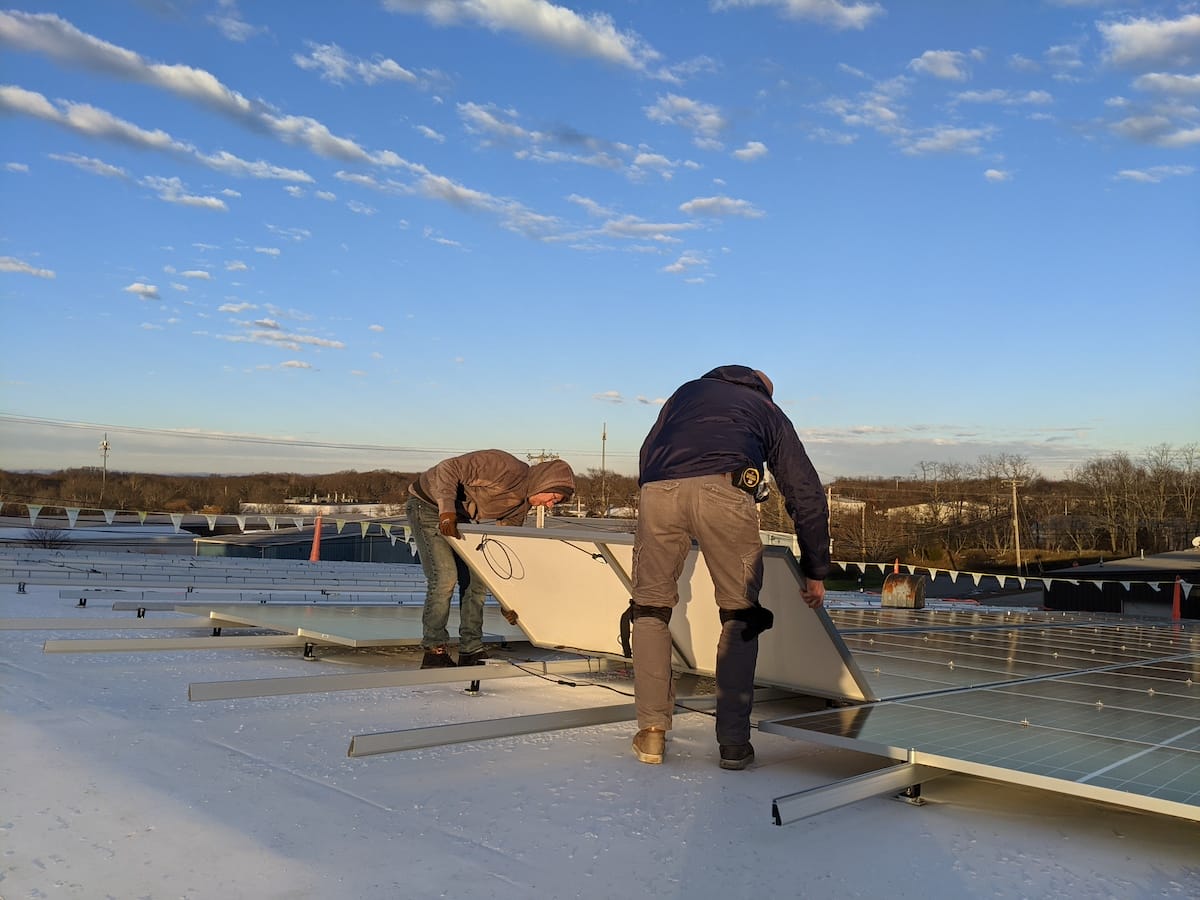 Solar installers lower panel on to racking on roof at sunset